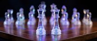 Glass chess set with transparent king and queen pieces on wooden board against dark background for strategic thinking and intellectual games.