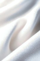 Soft white silk fabric with gentle folds creating subtle shadows and highlights, macro photography reveals delicate texture and shimmering surface.