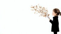 Young Asian woman in black turtleneck sweater blowing on dried flowers creating artistic effect against white background, minimalist style composition.