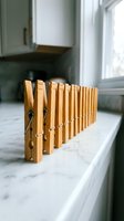 Wooden clothespins lined up in a row on a marble countertop near a bright window in a modern kitchen interior.