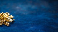 Golden metallic flower brooch on dark blue textured background with selective focus and copy space for luxury jewelry presentation.