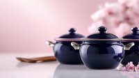 Navy ceramic cooking pots with lids on pink background with cherry blossom flowers, wooden spoon. Minimalist Asian cuisine and tableware composition.
