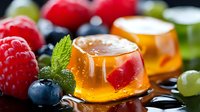 Orange jelly dessert with fresh berries and mint leaves on dark background, selective focus on translucent gelatin cubes garnished with fruits.