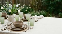Elegant outdoor dining table setting with neutral ceramic dinnerware and fresh white flowers for spring entertaining and garden party occasions.