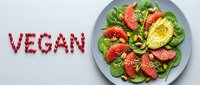 Fresh vegan salad with grapefruit, avocado, spinach, and nuts on a plate, with the word vegan made from pomegranate seeds on a light background.