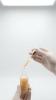 Scientist hands in latex gloves using dropper to add golden serum into glass vial in sterile laboratory environment for cosmetic research and development.