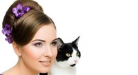 Young woman with brown hair styled in updo with purple flowers, holding black and white cat, isolated on white background for portrait and pet photography use.