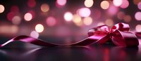 Elegant burgundy satin ribbon bow with flowing curves against dark surface, pink and golden bokeh lights creating romantic festive atmosphere.