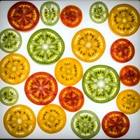 Colorful tomato slices in red, green and yellow varieties arranged on white background. Fresh organic vegetables for healthy cooking and food photography.