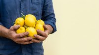 Man in denim shirt holding fresh yellow lemons in hands against neutral background. Suitable for food, agriculture, healthy eating and lifestyle content.