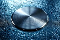 Brushed metallic steel disc on wet blue textured surface with water droplets and circular pattern reflection creating dramatic industrial atmosphere.