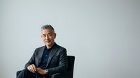 Mature man with gray hair and beard, wearing dark blazer and blue shirt, seated against white background for corporate portraits and business headshots.