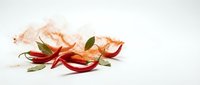 Red chili peppers with green leaves and spice powder scattered on white background, isolated culinary ingredients for cooking and seasoning applications.