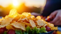 Crispy golden potato chips piled high with fresh lettuce garnish against warm sunset background, creating appetizing snack presentation with natural lighting.