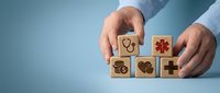 Male hands arranging wooden blocks with healthcare icons including heart, medical cross, and stethoscope symbols on blue background for health insurance and wellness concepts.