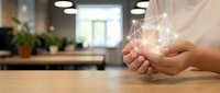 Hands holding glowing geometric network wireframe on wooden desk in modern office environment with plants and blurred background.