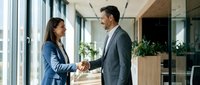 Professional businesswoman and businessman shaking hands in modern office corridor during successful meeting or partnership agreement.