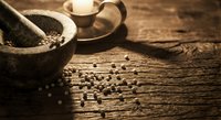 Stone mortar and pestle with scattered peppercorns on rustic wooden surface, traditional spice grinding tools for culinary preparation and cooking.