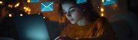 Young woman in orange sweater using smartphone at night with glowing email icons and bokeh lights floating above, creating digital communication concept.