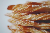 Flaky layers of golden pastry dusted with coarse salt crystals in macro view, showing delicate textures and warm tones of freshly baked puff pastry.