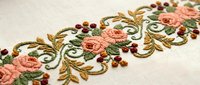 Elegant floral embroidery with pink roses and golden leaves on cream fabric. Decorative needlework border perfect for textile design and crafting projects.
