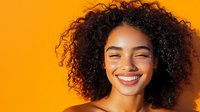 Young African American woman with natural curly hair and bright genuine smile against vibrant orange background, expressing joy and confidence in casual portrait.