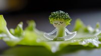 Whimsical broccoli character with transparent wings resting on green leaf, creative food photography with natural lighting and shallow depth of field.