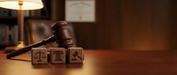 Wooden gavel and legal symbol blocks on desk in law office with warm lighting for attorney and judicial concepts.