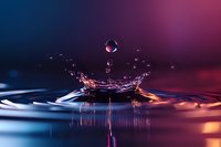 Water droplet creating splash with crown formation on liquid surface against vibrant blue and pink gradient background for creative projects.
