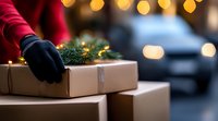 Hands in black gloves arranging kraft boxes decorated with pine branches against blurred holiday lights background, creating cozy Christmas delivery atmosphere.