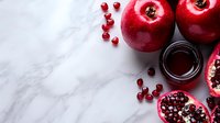 Fresh red pomegranate and apples with juice on white marble background. Scattered arils create natural composition with copy space for food styling.