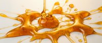 Liquid amber or honey splashing and dripping with dynamic motion, creating an abstract golden splash pattern against a white background for design and creative projects.