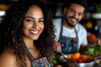 Young African American woman with curly hair smiling in kitchen while cooking with male partner wearing apron, preparing healthy meal together in casual home setting.