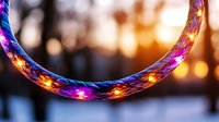 Glowing LED hula hoop illuminated with vibrant pink, blue and orange lights against blurred winter sunset background creates magical light trail effect.