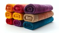 Stack of vibrant rolled bath towels in orange, yellow, red, purple, beige and turquoise colors on white background, clean fresh cotton terry cloth textile.