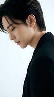 Young Asian man in black sweater looking down thoughtfully against white background for lifestyle and fashion content.