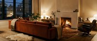 Luxury living room with burnt orange velvet sofa, fireplace, warm lighting, and city skyline view through floor-to-ceiling windows for upscale interior design projects.