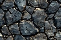 Dark cracked stone surface with rough angular shapes and deep crevices creates natural mosaic pattern, dramatic lighting highlights texture and shadows.