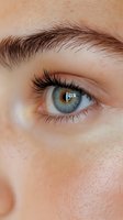 Close-up of a light blue eye with long eyelashes and defined eyebrow, showing natural skin texture and subtle window reflection in iris, suitable for beauty content.