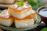 Sweet rice cakes with caramelized sugar topping garnished with fresh mint leaves on green ceramic plate, traditional Asian dessert served with syrup.