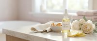 Young woman with fair complexion applying facial serum on bathroom counter surrounded by cream roses, natural skincare bottles, and spa essentials for beauty and wellness routines.