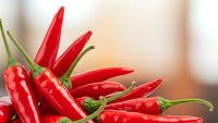 Fresh red hot chili peppers with green stems arranged on wooden surface for cooking and spicy food preparation in kitchen setting.