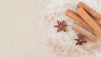 Aromatic cinnamon sticks and star anise scattered on light beige background with flour dusting, creating rustic baking composition for food photography.
