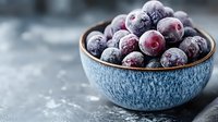 Fresh frozen cranberries covered in frost in blue ceramic bowl on rustic wooden background. Close up view with selective focus and copy space.