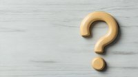 Golden question mark symbol on light gray marble background, minimalist design concept for FAQ, help, or problem solving solutions.