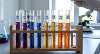 Laboratory scientist conducting chemical analysis with colorful test tubes in wooden rack for research and experimentation in modern lab setting.