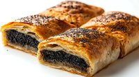 Freshly baked poppy seed strudel with flaky puff pastry layers, sprinkled with seeds on golden brown crust, cut to show dense filling on white background.