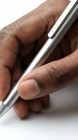 Close-up of a dark-skinned hand holding a sleek silver metallic pen, ready to write, on a white background.