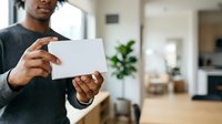 Man of African descent holding blank white card in modern home interior, suitable for business messaging, advertising, and promotional content.