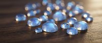 Clear blue glass marbles scattered on rustic wooden surface with warm golden lighting creating magical bokeh effects for decorative design projects.